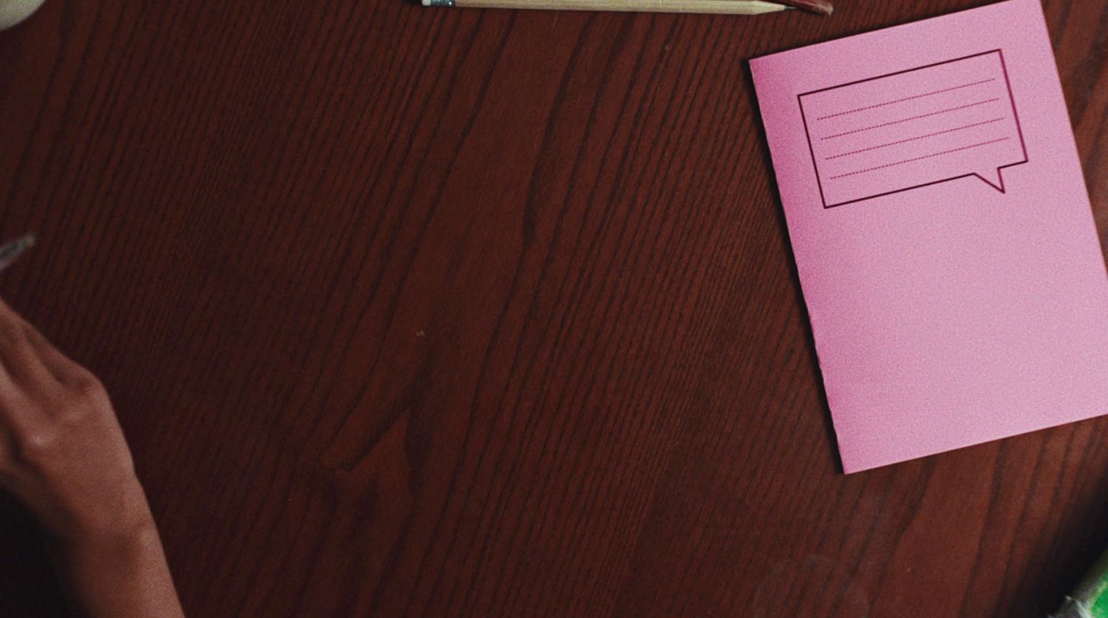 a person writing on a piece of pink paper