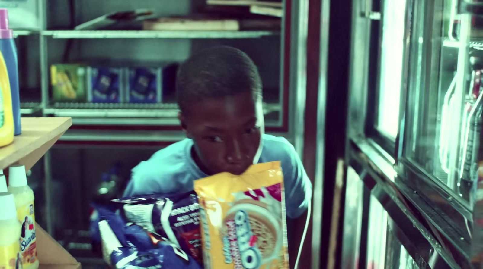 a young boy holding a bag of chips in front of a refrigerator