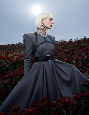 a woman in a gray dress standing in a field of flowers