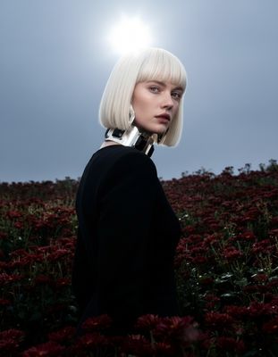 a woman with white hair standing in a field of flowers