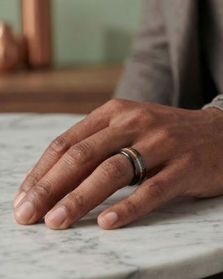 a man's hand with a wedding ring on a marble table