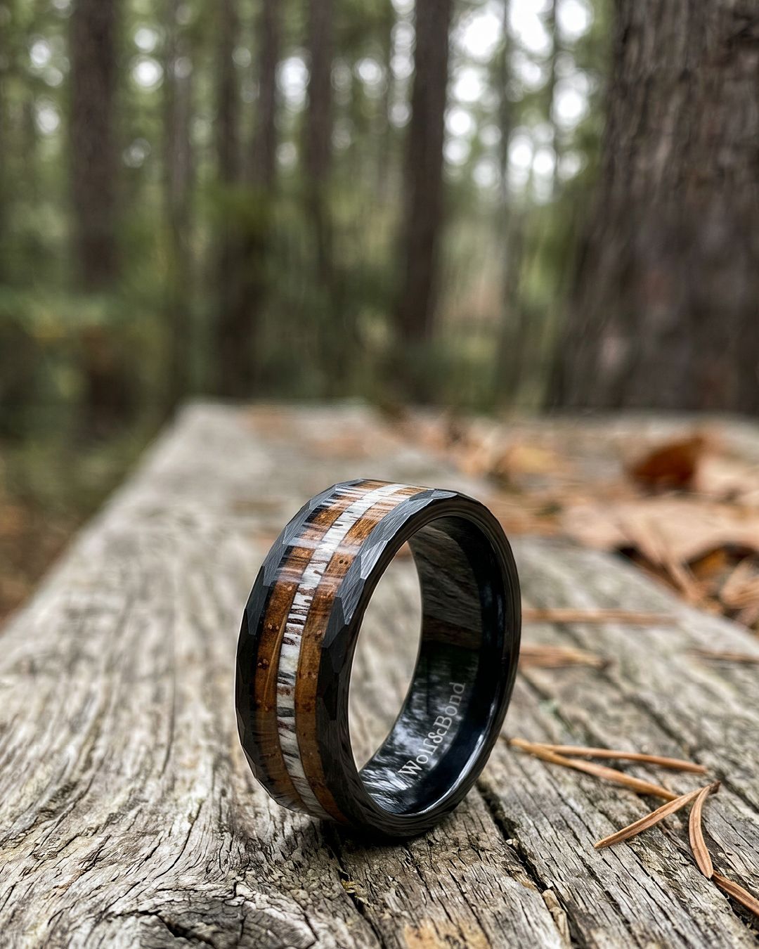 a wedding band with a wood inlay is sitting on a log in the woods