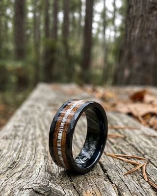 a wedding band with a wood inlay is sitting on a log in the woods