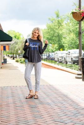 a woman standing on a brick walkway wearing a black shirt and striped pants