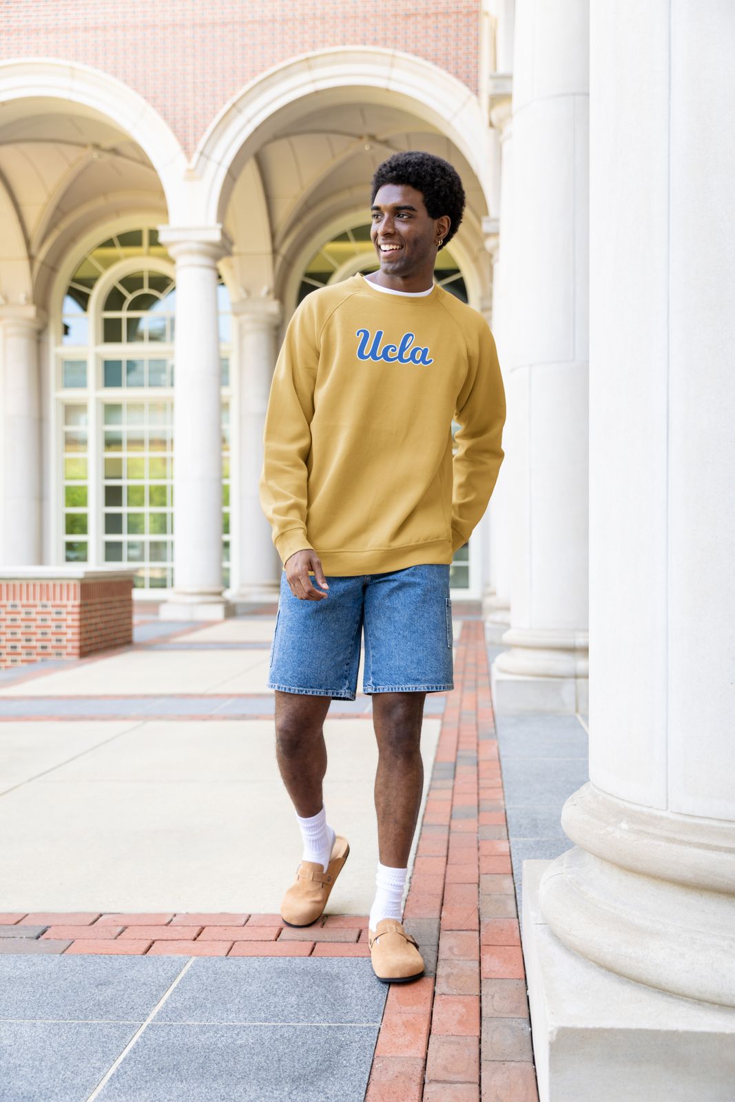 a man standing in front of a building wearing a yellow sweater and blue shorts