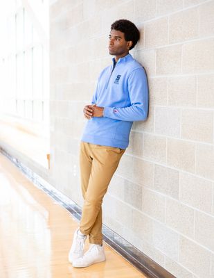 a man leaning against a wall with his hands in his pockets