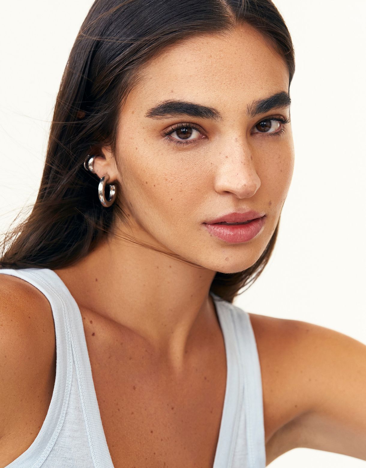 a woman wearing a white tank top and earrings