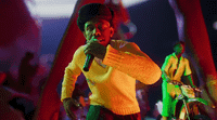 a man in a yellow sweater singing into a microphone