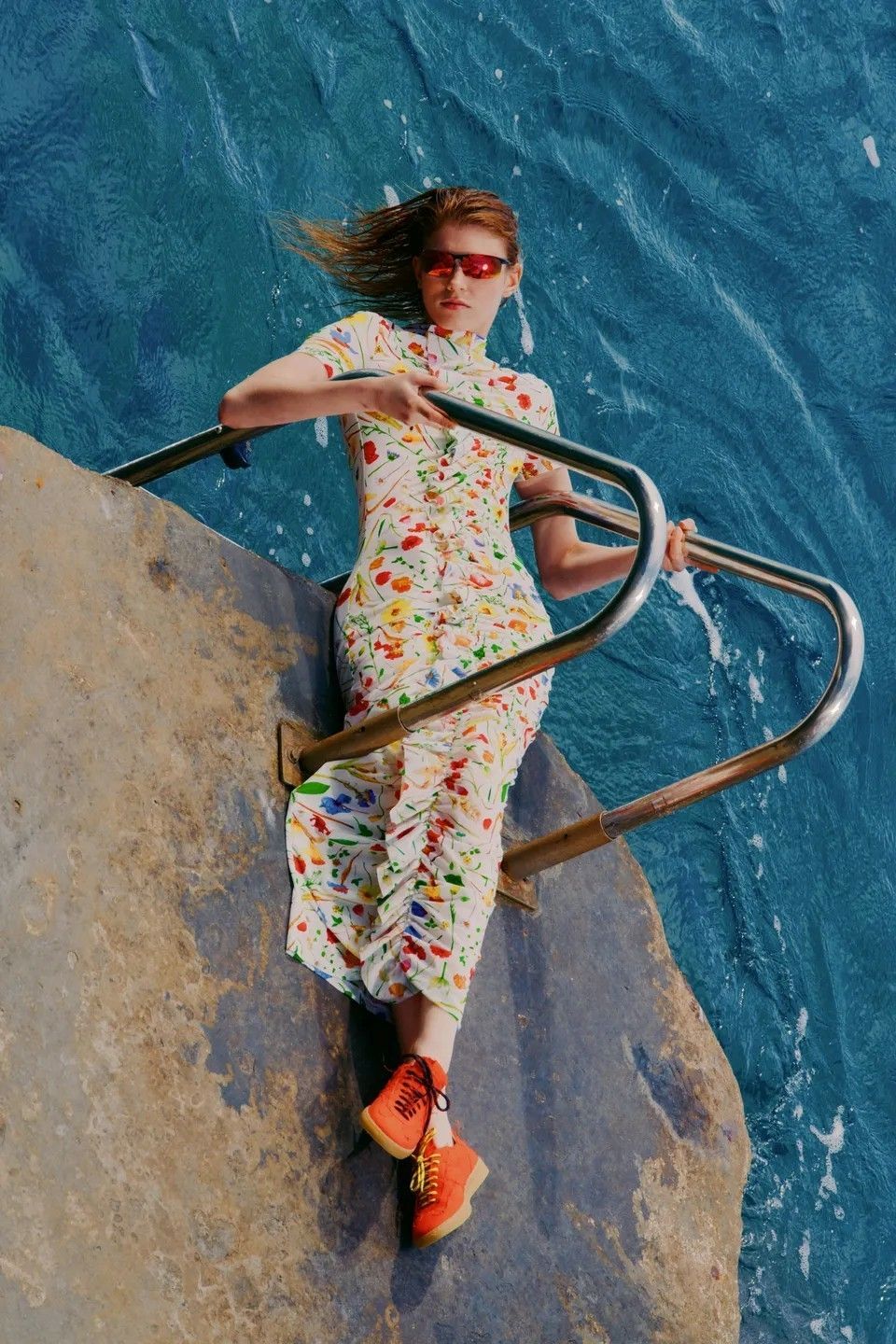 a woman in a colorful dress sitting on a rock next to the ocean