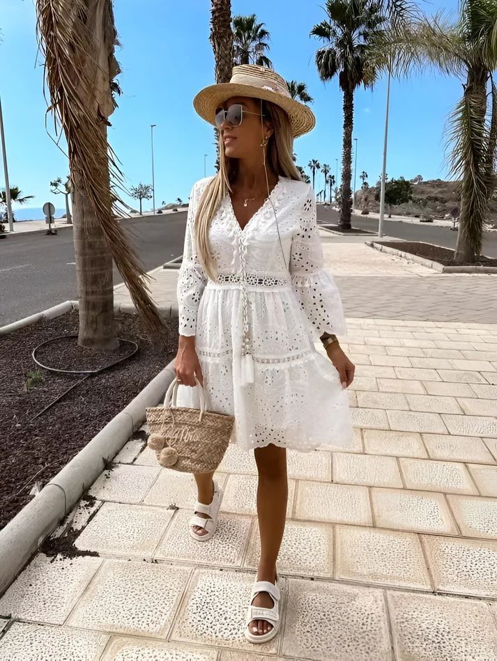 a woman in a white dress and hat walking down a sidewalk