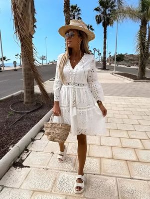 a woman in a white dress and hat walking down a sidewalk