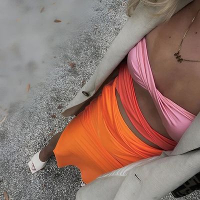 a woman in an orange and pink dress sitting on the ground