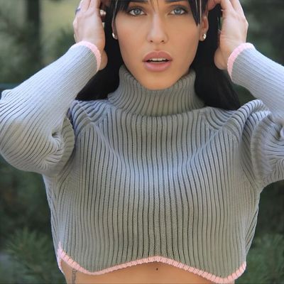 a woman in a gray sweater holding her hair up to her head