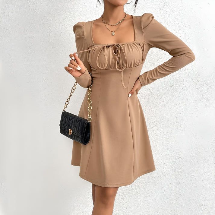 a woman in a tan dress holding a black purse