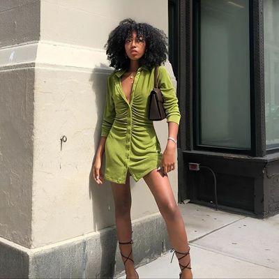 a woman in a green dress leaning against a building