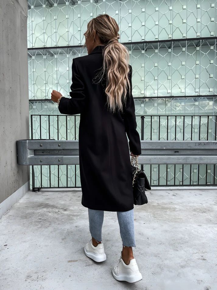 a woman in a black coat is standing on a bench