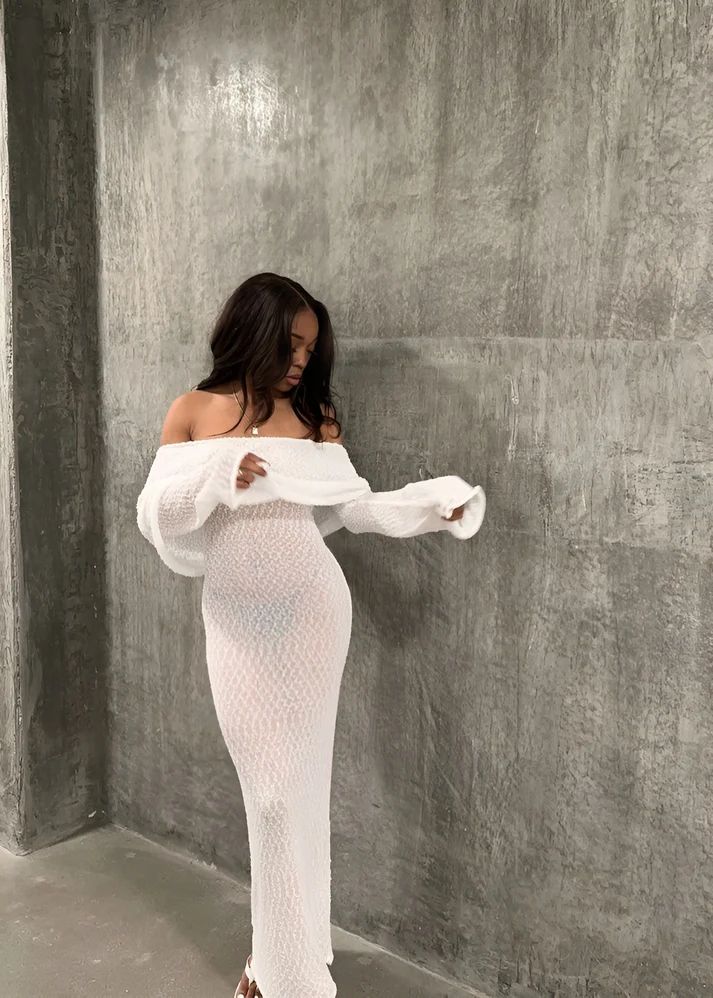 a woman in a white dress leaning against a wall