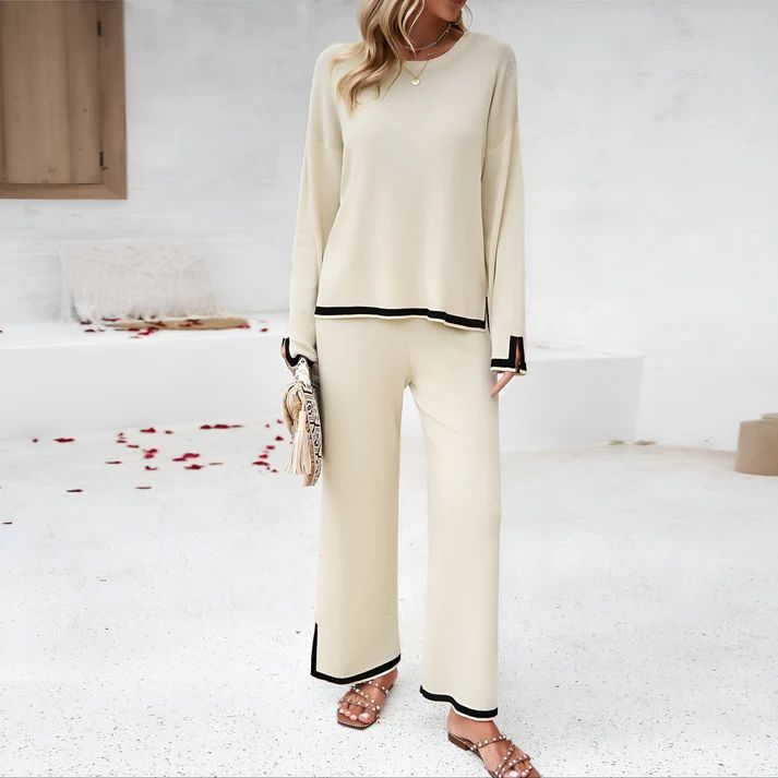 a woman standing in a white room wearing a pair of pants and a sweater