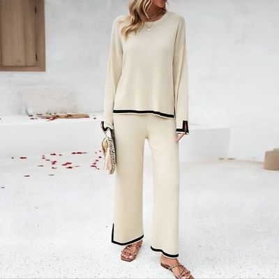 a woman standing in a white room wearing a pair of pants and a sweater