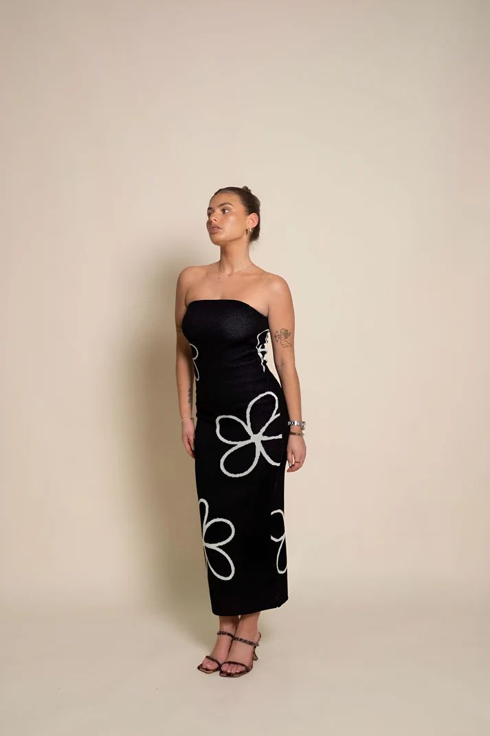 a woman wearing a black dress with white flowers on it