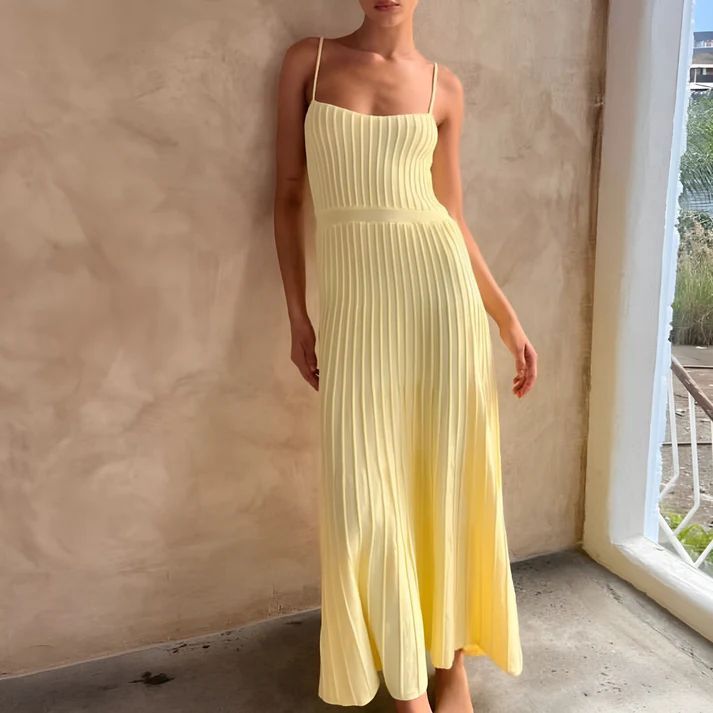 a woman in a yellow dress leaning against a wall