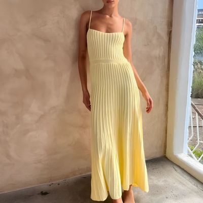 a woman in a yellow dress leaning against a wall