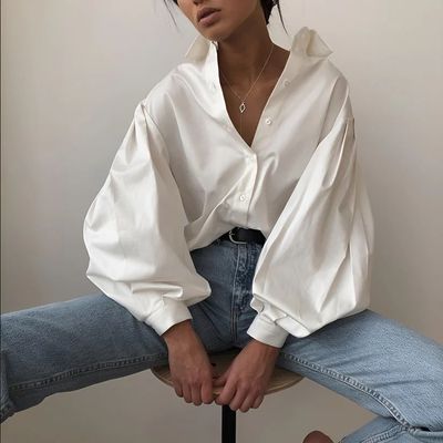 a woman sitting on a stool wearing a white shirt and jeans