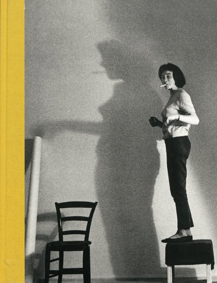 a black and white photo of a woman standing on a chair