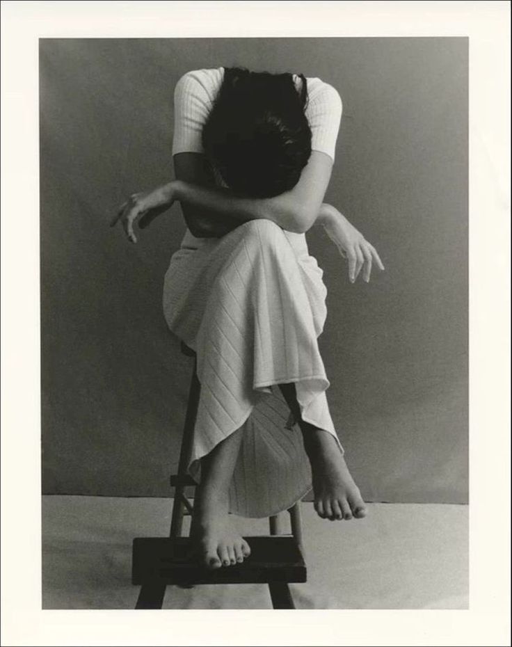 a black and white photo of a woman sitting on a stool