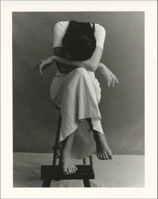 a black and white photo of a woman sitting on a stool