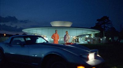 two men standing next to a car in front of a building