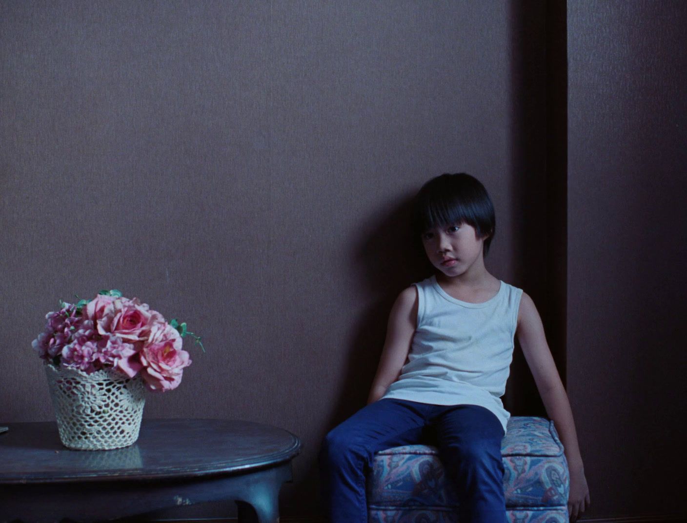 a young girl sitting on a chair next to a table with a vase of flowers