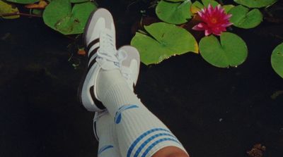 a person's feet in a pair of white shoes next to water lilies