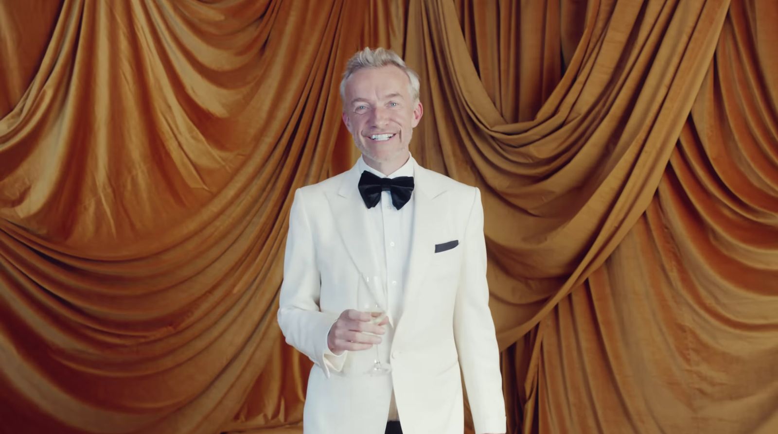 a man in a white tuxedo standing in front of a curtain