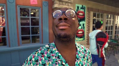 a man wearing glasses standing in front of a building