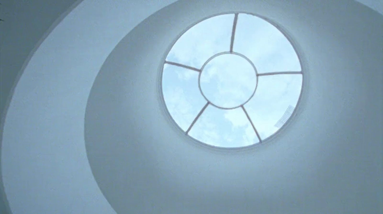 a round window in a white wall with a sky view