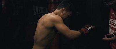 a man with no shirt on standing next to a punching bag