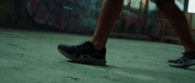 a person's legs and shoes in front of a wall with graffiti