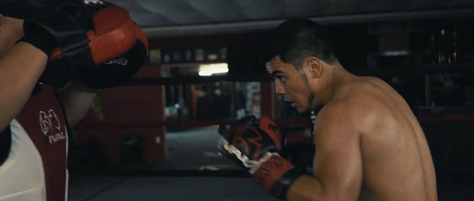 a man with no shirt on standing next to a punching bag