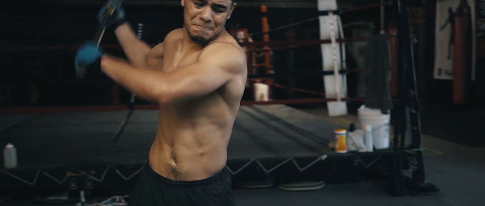 a shirtless man holding a tennis racquet in a gym