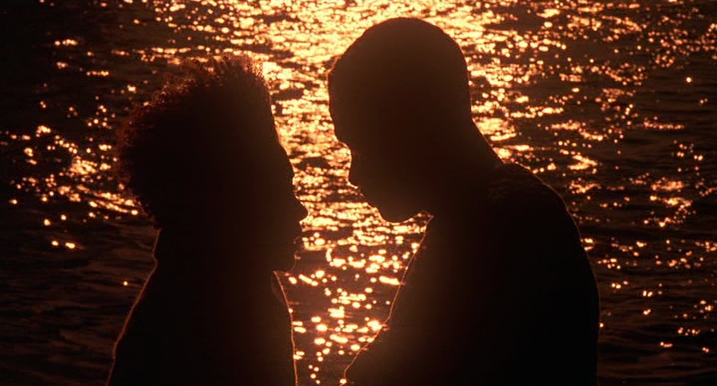 two people standing next to each other in front of a body of water