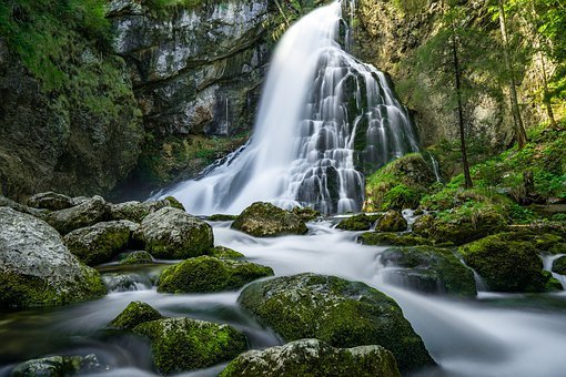 a waterfall in a forest with mossy rocks