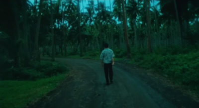 a man walking down a dirt road in the middle of a forest