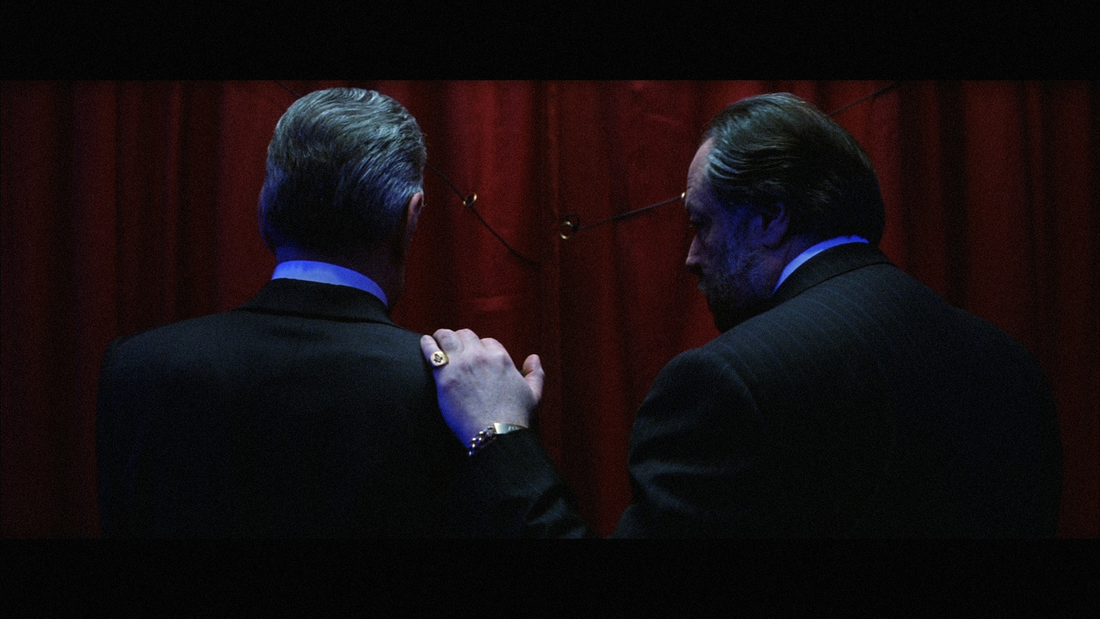 a couple of men standing next to each other in front of a red curtain