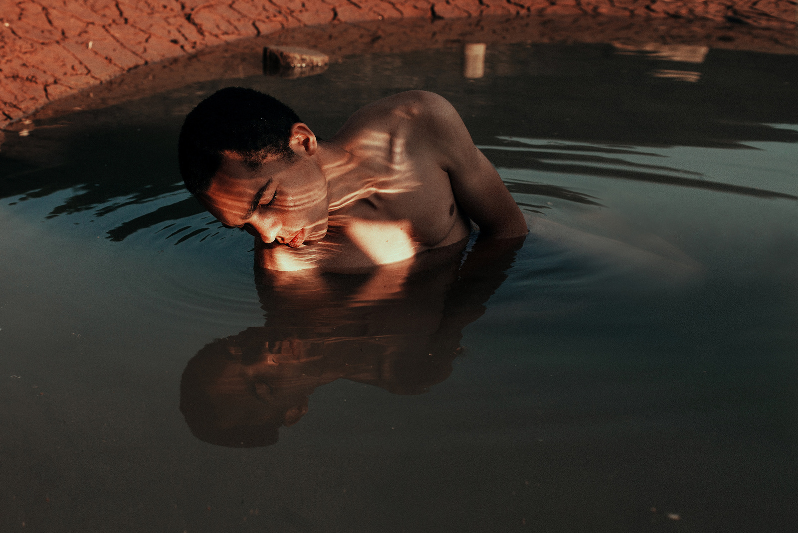 a man in a body of water next to a brick wall