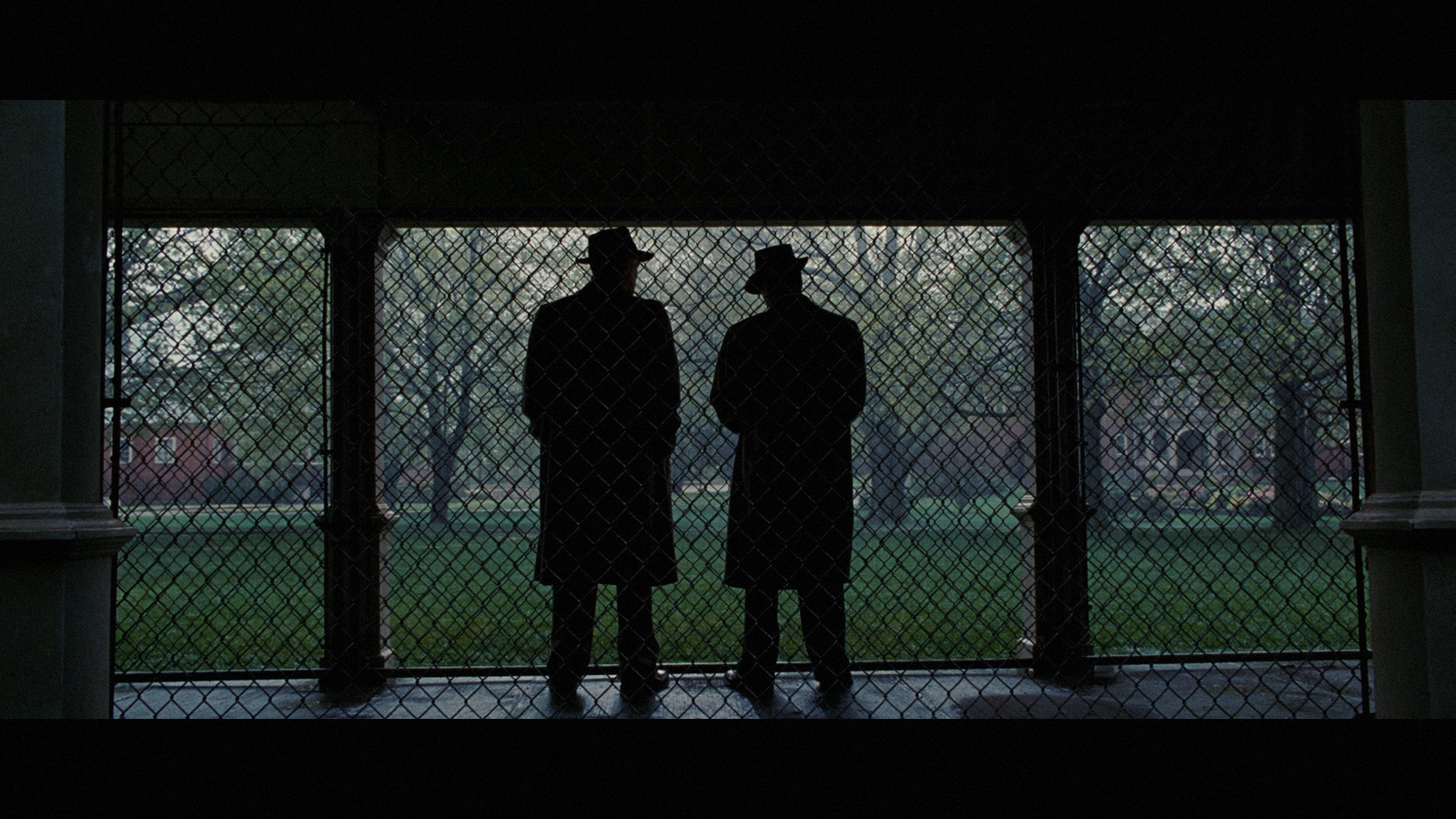 a couple of men standing next to each other in front of a fence