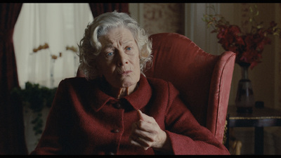 an old woman sitting in a red chair with a cigarette in her mouth