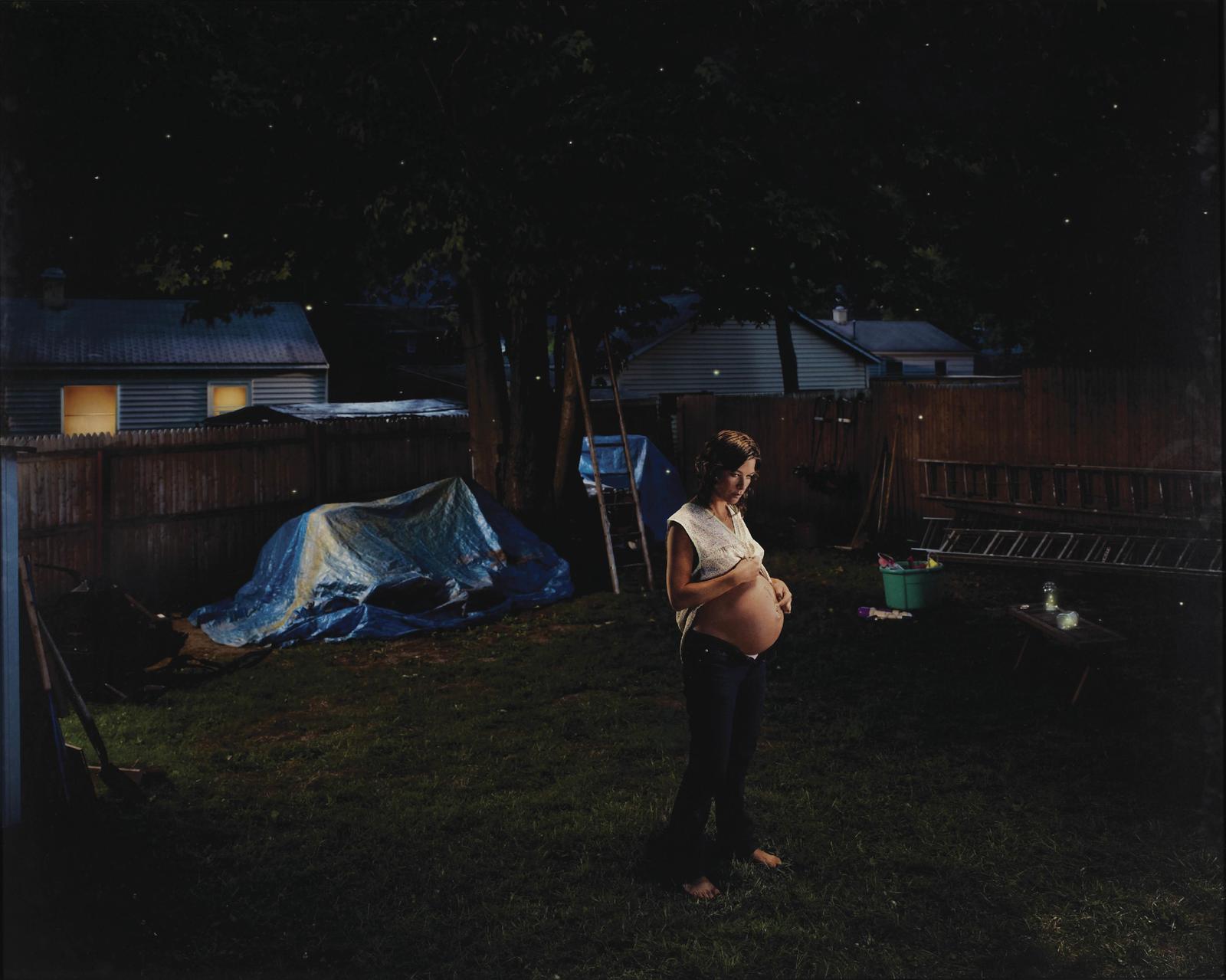 a pregnant woman standing in a yard at night