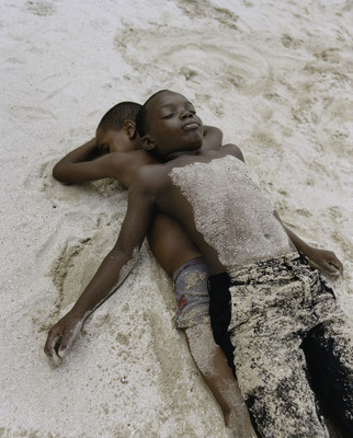 a couple of kids laying on top of a sandy beach