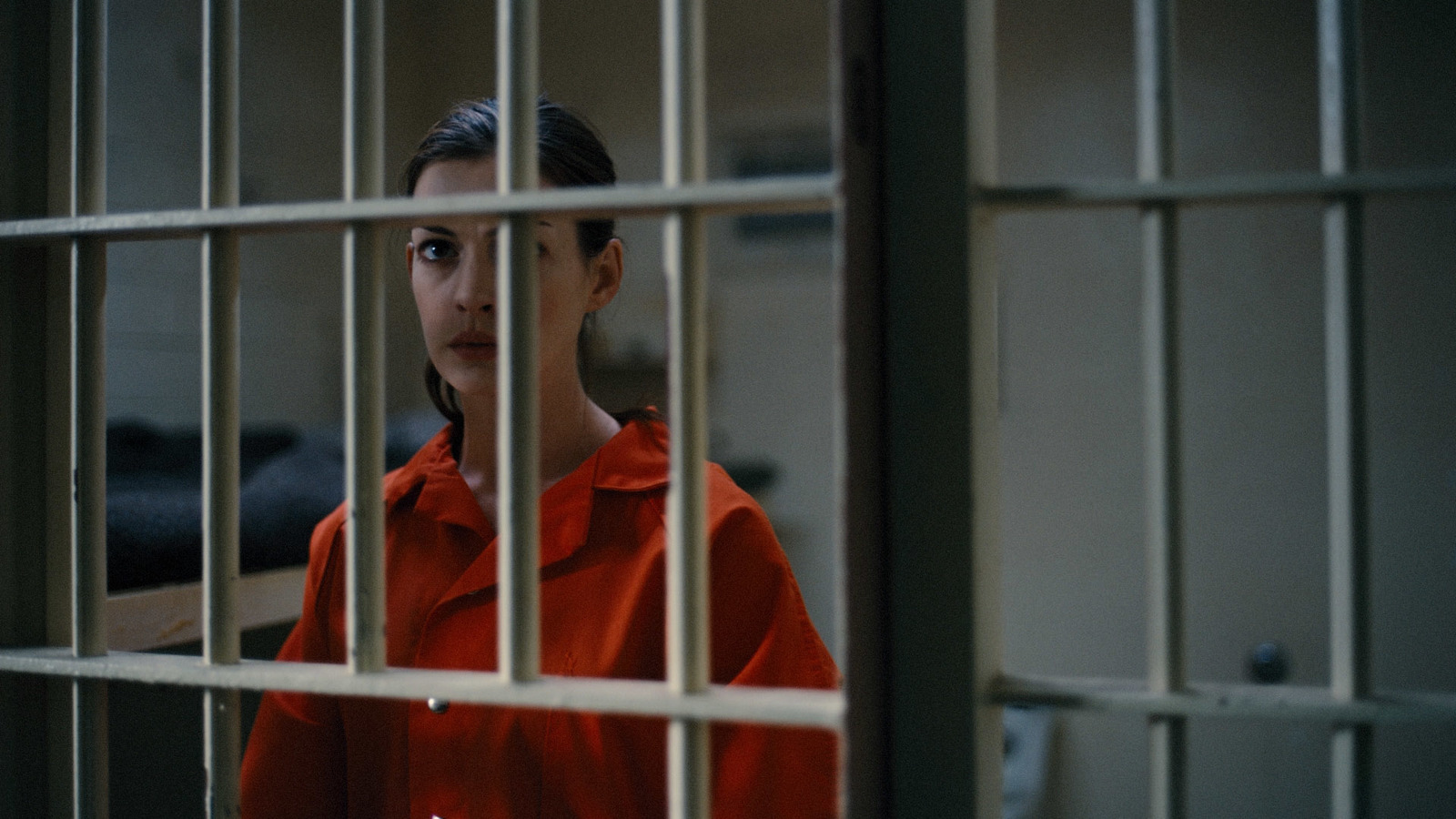 a woman in a red jacket behind bars in a jail cell